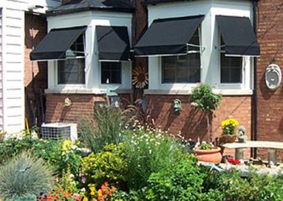 2 story brick home with black awnings over windows